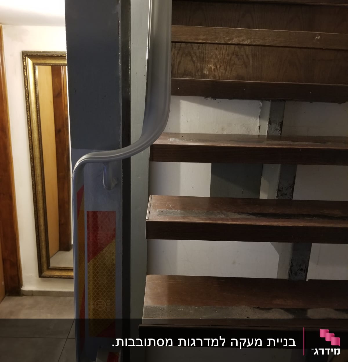 מראה במסגרת זהב ליד גרם מדרגות עץ